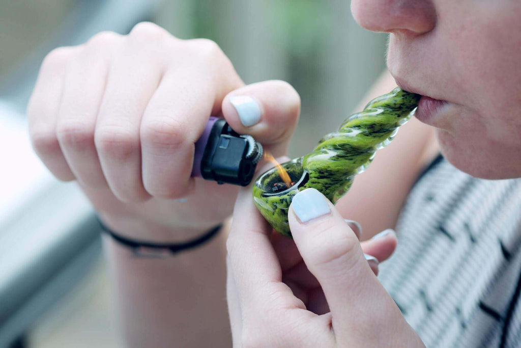 person lighting a green glass pipe