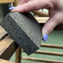 Hand sanding down the outer edge of the chair with a sandpaper block.