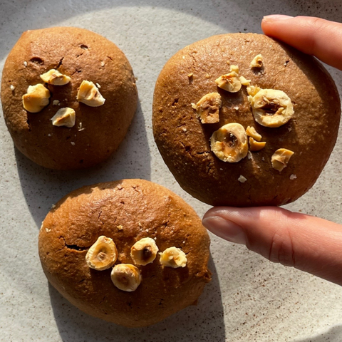 Mano che tiene un biscotto brownie vegano, due biscotti brownie su piatto grigio 