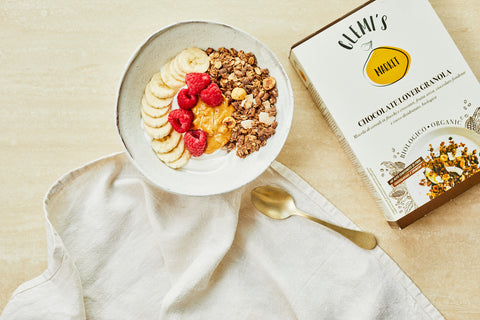 Yogurt bowl with chocolate lover granola, raspberries, bananas, with gold spoon and kitchen cloth