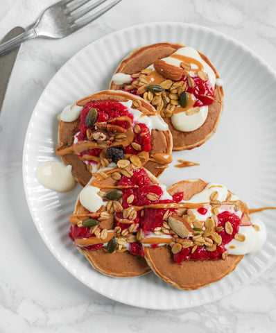 Pancakes su piatto bianco con yogurt, marmellata ai lamponi e granola