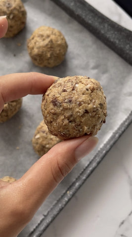 Due dita tengono una pallina di biscotti con granola con sfondo una teglia