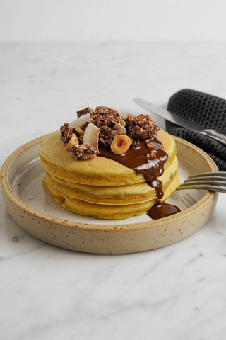 Pancakes con granola su piatto bianco con forchetta e coltello