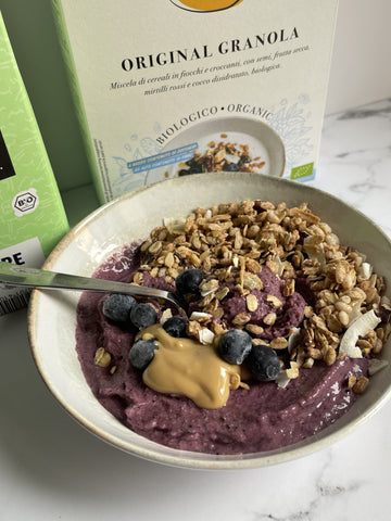 Piatto con smoothie bowl con mirtilli, Original Granola Clemi's Market, burro di arachidi, con cucchiaino argento, su sfondo scatola granola