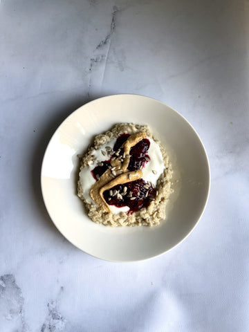 Piatto bianco con porridge cremoso, yogurt, marmellata di frutti di bosco, burro di arachidi e semi di girasole