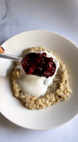 Piatto bianco con porridge cremoso, yogurt, marmellata di frutti di bosco e cucchiaio argento