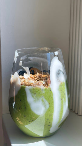 Glass with green smoothie with spinach and avocado, granola and blueberries