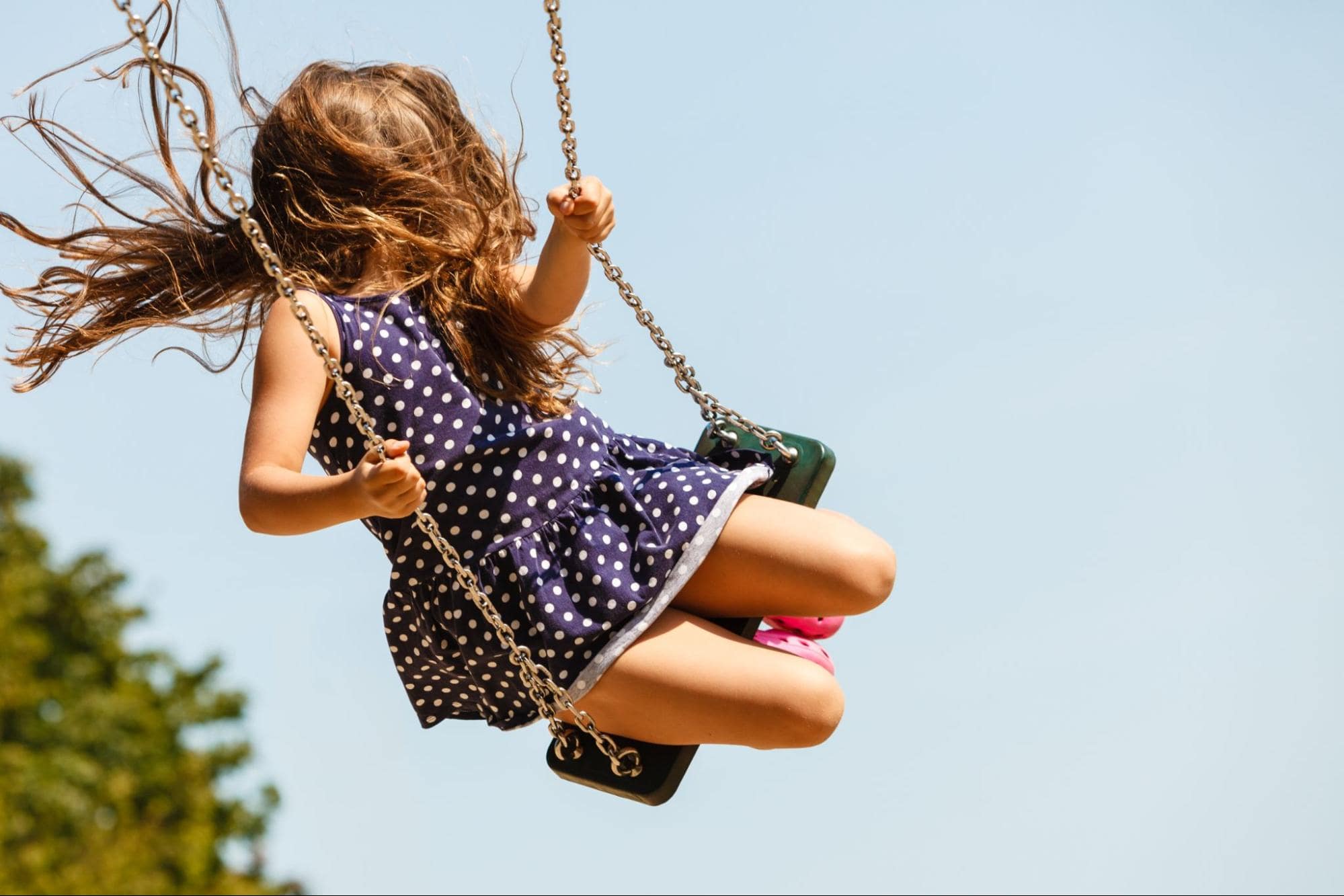 A young girl in a summer dress swinging on a green swing set.