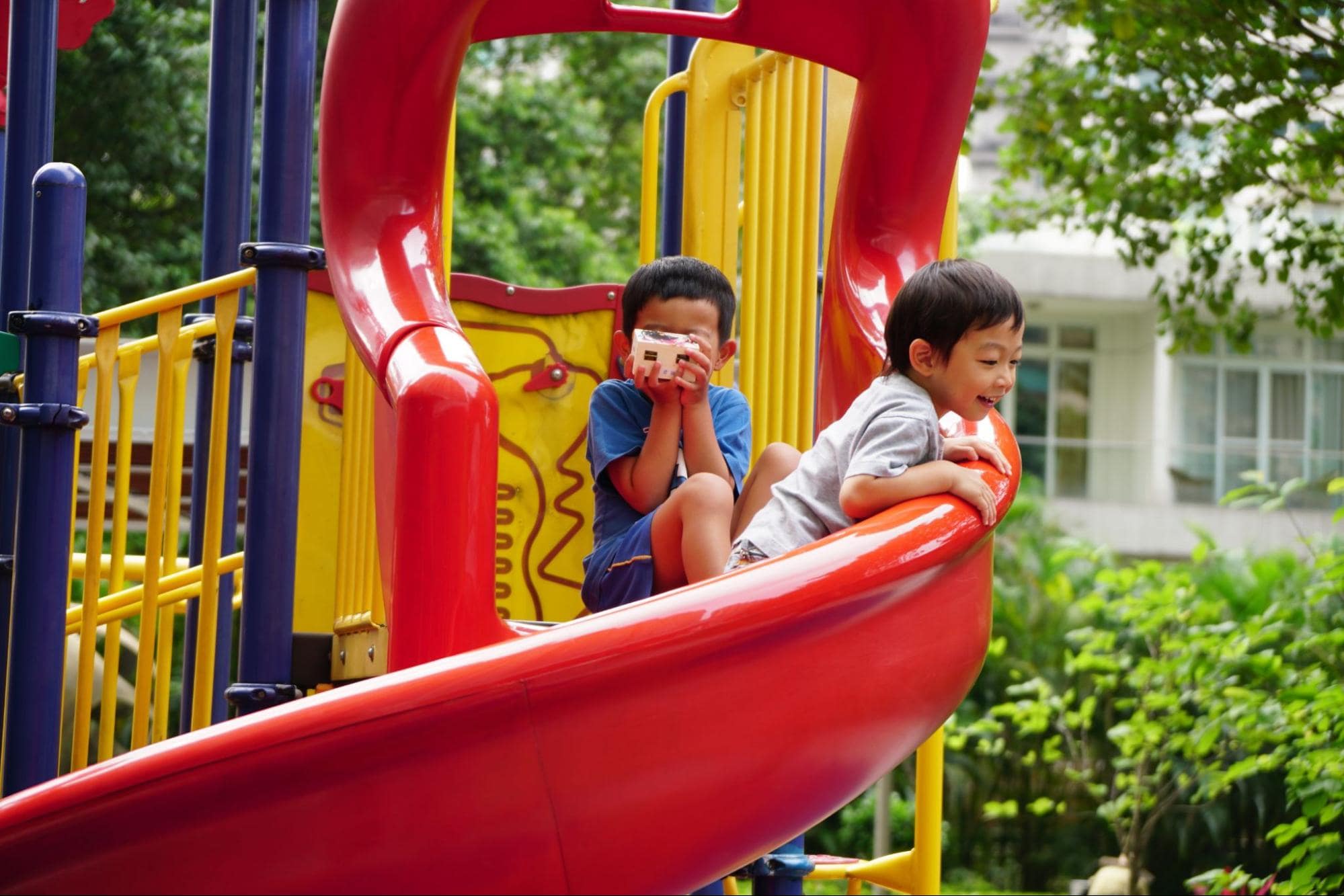 Two children playing on a Playset and coming down a slide.