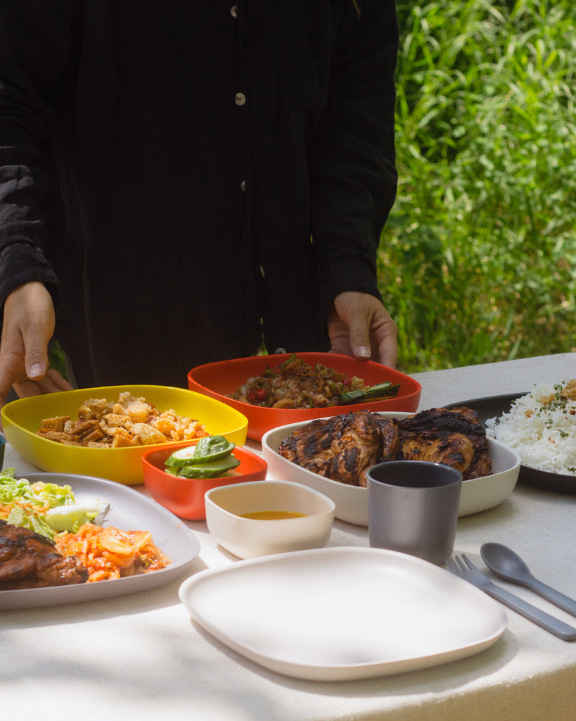 Someone setting down a serving plate of Bicol Express next to a plate of Tokwa't Baboy, alongside Inihaw na Manok (BBQ Chicken) and rice