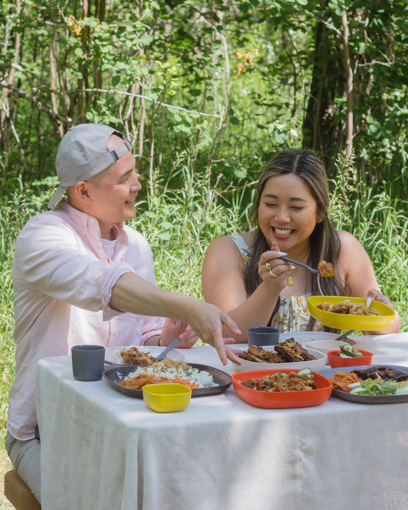 Bjorn and Rachel share food from Lola's Cluck + Oink at a picnic with EKOBO Gusto plates, bowls, and other tableware