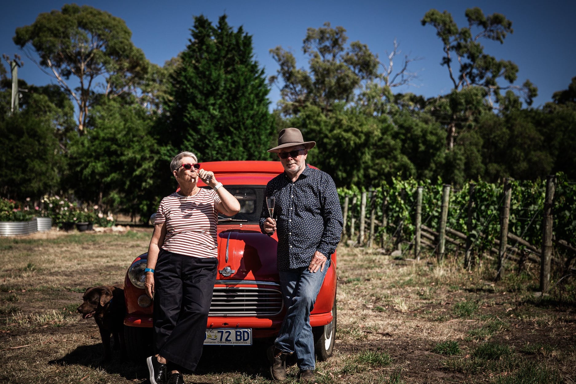 Lyn and Michael Rochford sip their sparkling wine in front of a red van at the vineyard