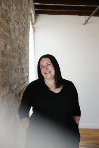 A photo of Bethany, the artist behind Passing Notes. She is wearing a black dress and is in an industrial building.