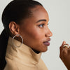 A woman in a turtleneck showcases Figure Oversized Hoops, sterling silver earrings set with white sapphire gemstones, highlighting their elegant curves.