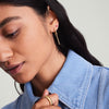 Woman adjusting collar, showcasing Gemstone Mini Studs in 14k gold. Close-up highlights the intricate design and punchy tones of the earrings.