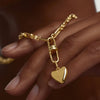 Hand holding a gold chain with a puffy heart charm pendant, highlighting the intricate design and craftsmanship.