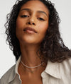 Micro Pearl Necklace on a woman with curly hair, wearing a white shirt. The necklace is handcrafted in 14k gold with freshwater pearls.