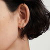 Close-up of a woman's ear adorned with Bezel Lab Grown Diamond Huggies in 14k solid gold, featuring sparkling, ethically produced lab grown diamonds.