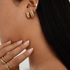 Woman wearing Chunky Medium Hoops, featuring clicker closure for comfort. Close-up shows gold earrings stacked stylishly, highlighting their pillowy design.