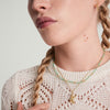 Woman with braided hair wearing a handcrafted Beads Necklace made of 18k gold vermeil and precious gemstones, paired with a white sweater.