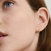 Close-up of a woman's ear wearing Pavé Diamond Huggie Hoops, featuring handcrafted recycled 14k solid gold and pavé diamonds.