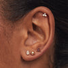 Close-up of a person's ear wearing a Piercing Studio - Garnet Lotus Flat Back Stud, featuring a 14k gold setting with garnet stones and titanium backing.