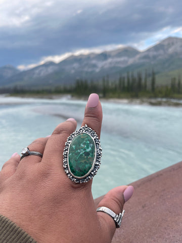 statement sterling silver ring featuring large chrysocolla gemstone on index finger pointing at the lake and mountain