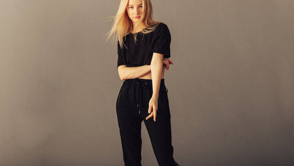 A blonde woman stands wearing an all black outfit, complete with a t-shirt and high end sweatpants. The outfit is made from sustainable bamboo fibers.