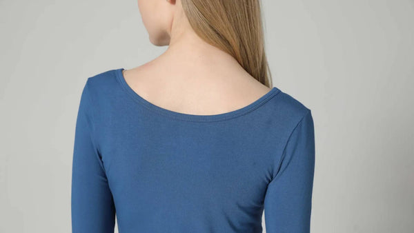 A blonde woman stands with her back facing the camera while wearing a blue long sleeve shirt made from sustainable bamboo fiber.