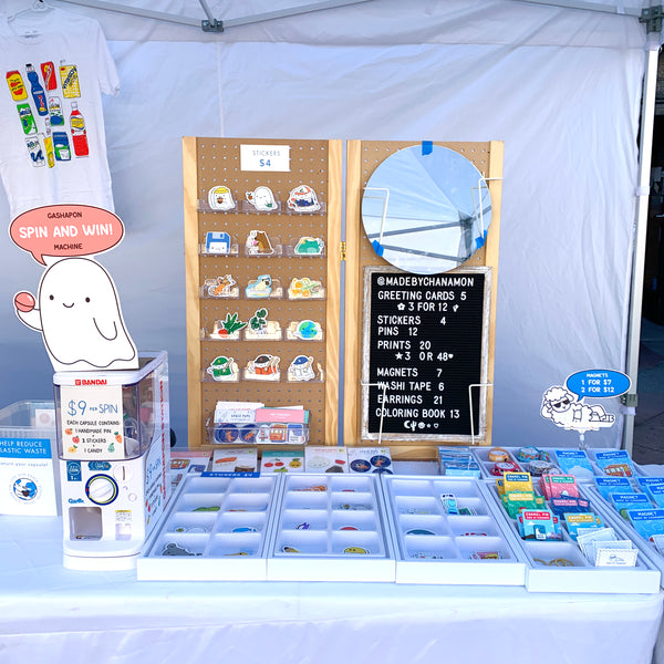 Photo of the sticker display set up. There is a pegboard with mounted holders and trays of stickers on the table.