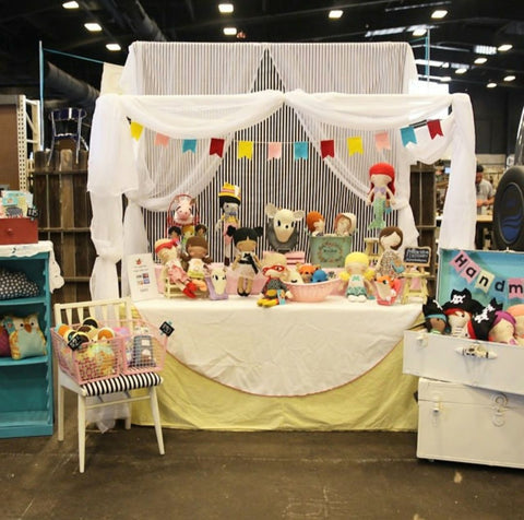 Craft show table with yellow and white table cloth, striped backdrop featuring dolls and faux taxidermy.  