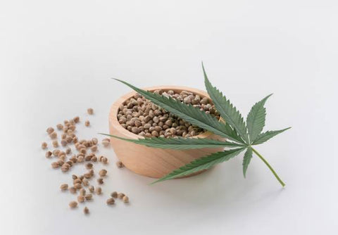 cuenco de bamboo con semillas de marihuana y una hoja de la planta