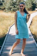 Frau steht in einem himmelblauen Leinenkleid auf einem Holzweg
