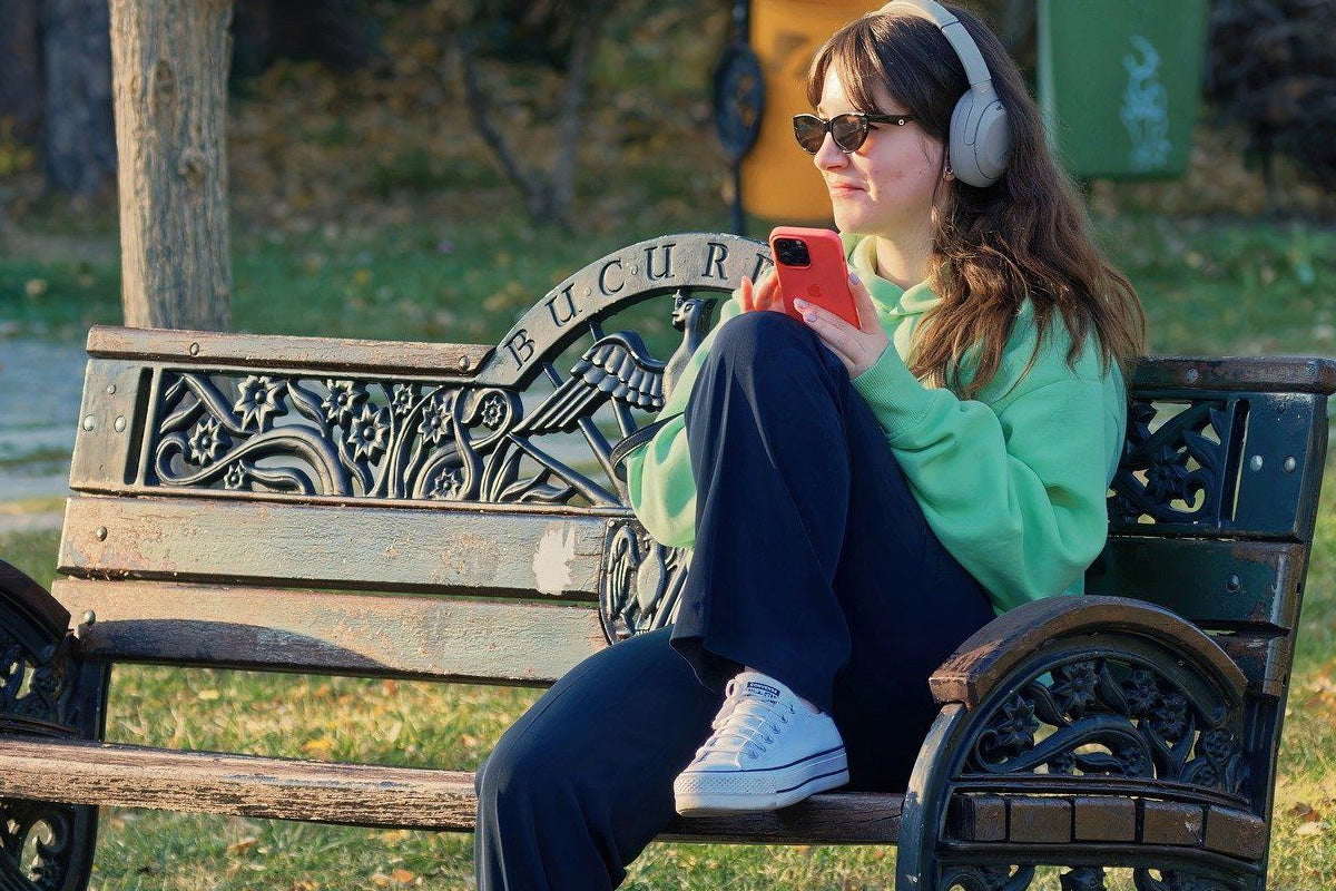 A woman chilling and relaxing on a bench park while listening to music on her phone