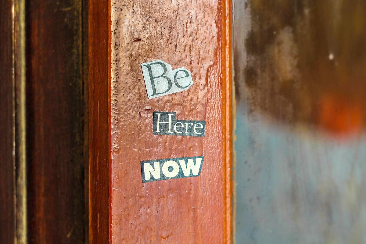 Motivational message "Be Here Now" adhered to a wooden surface