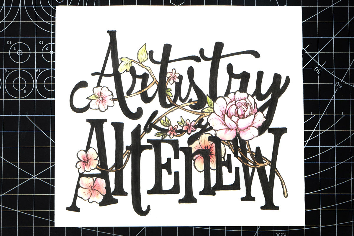 A lettering of "Artistry by Altenew" with floral accents and embellishments