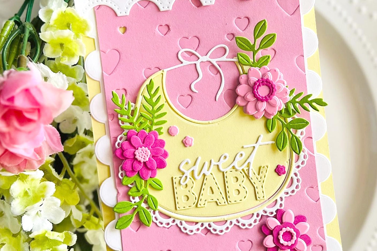 An extravagant pink baby card featuring a bib die cut and florals