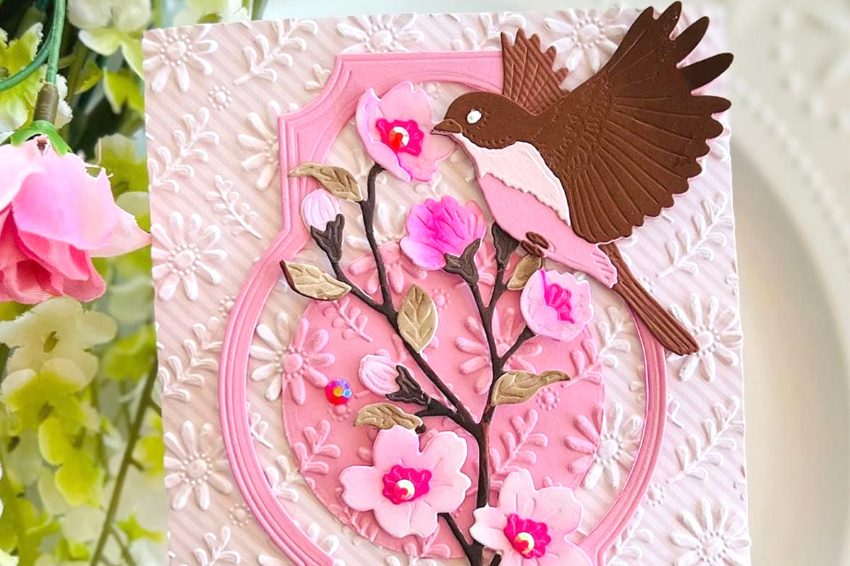 A pink card featuring cherry blossoms as focal points, accented with a brown bird die cut