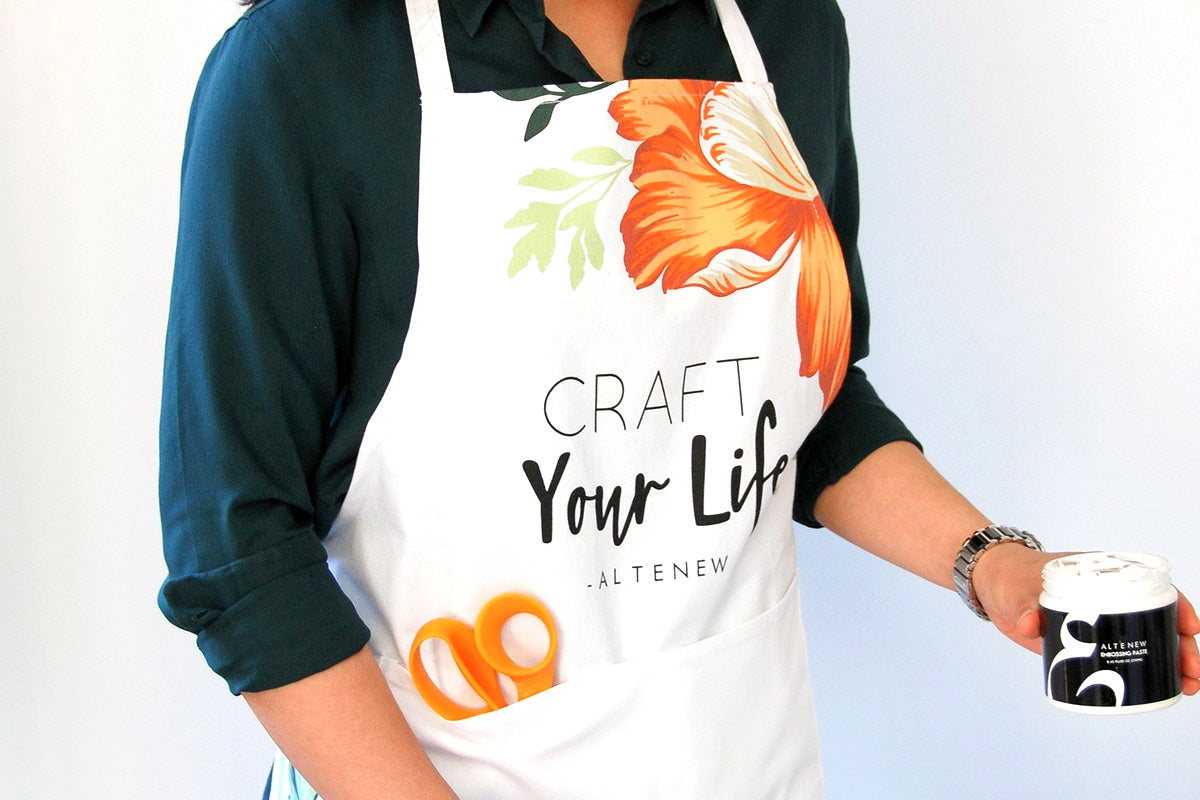 An artist in a Craft Your Life apron using Artistry's embossing paste to create mixed media art