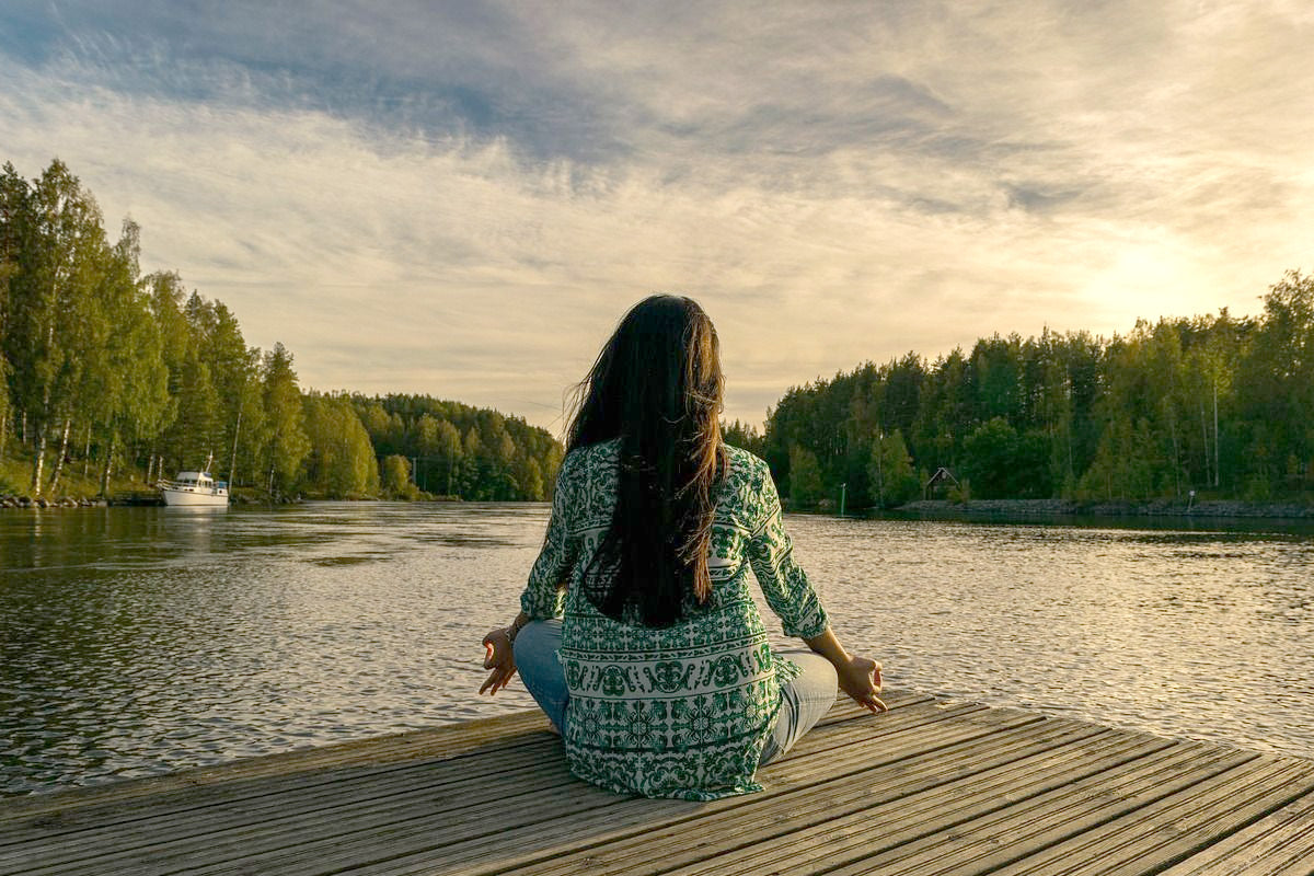 A woman sitting on a deck by the lake and meditating