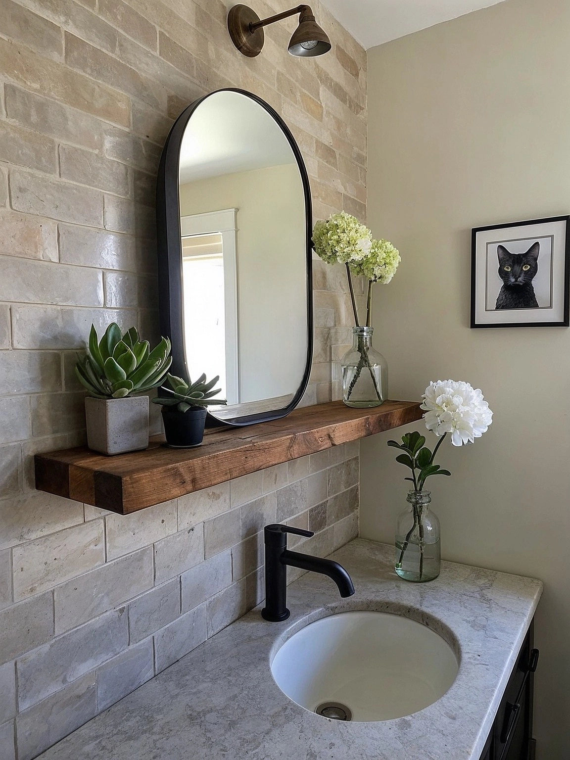 A small bathroom vanity with a floating wooden shelf beneath an arched mirror, featuring neutral-toned subway tile, black faucet, potted plants, and minimalist decor.