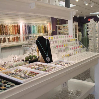 Sales floor showing wall rack of tubed seed beads and tables of jewelry making supplies.