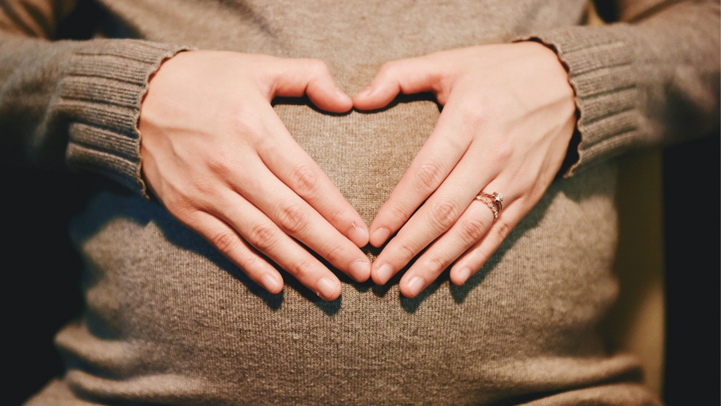 Photo d'une femme enceinte faisant avec ses mains un coeur sur son ventre