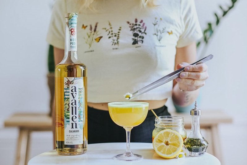 A woman preparing a glass of Avallen Calvados cocktail with honey, lemon and spices