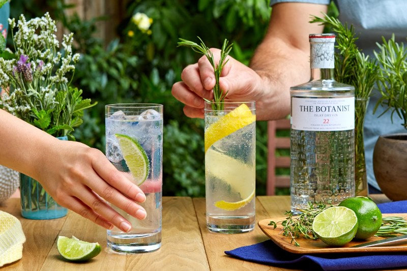 A bottle of The Botanist Gin with two glasses of mixed Gin and Tonic cocktails being served with lime slices