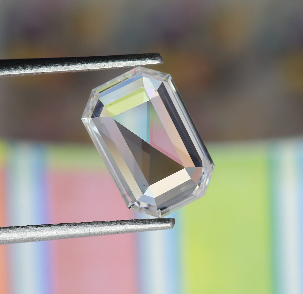 An emrald cut diamond with hints of blue, pink, and green refracting inside of it.