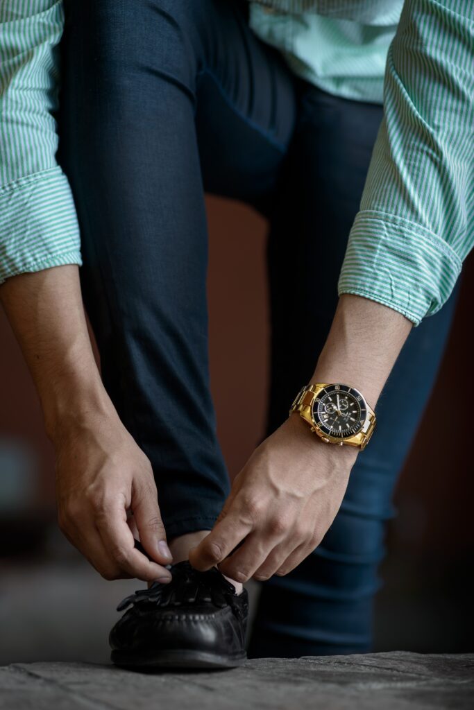 A man in business casual clothes tying his shoes with a rolex on his left wrist.