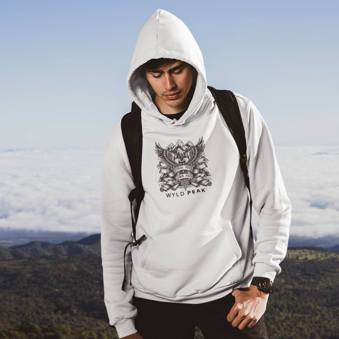 A man in a Wyld Peak organic Americana hoodie standing atop a scenic American mountain peak during a hike