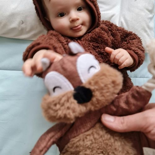 Bébé vêtu d’une combinaison marron jouant avec un doudou écureuil doux et souriant
