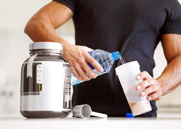 Aminoácidos; Persona sirviendo agua en un vaso con polvo, a lado un bote grande gris.